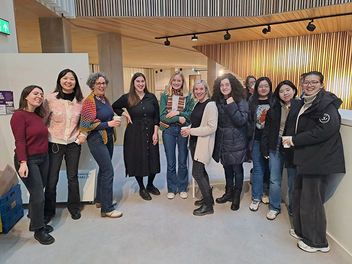 Rachel stood amongst a group of around 12 students stood in a semicircle, in a university building. They're all looking at the camera and smiling.